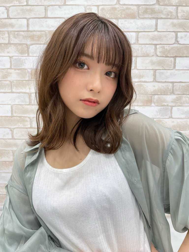 一位年輕女性，短髮微卷，穿著淺色上衣，坐在磚牆前，表情自然，展現出可愛和魅力。