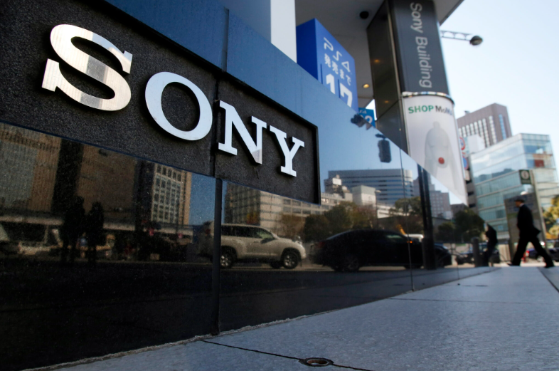 Close-up of the Sony logo on a building facade, with people walking by in the background.
