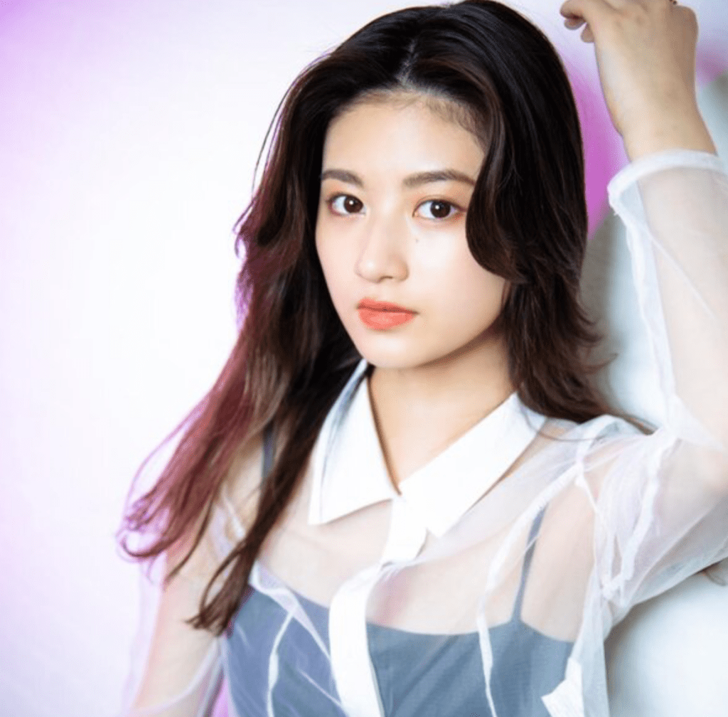 一位穿著淺色上衣的年輕女性，長髮披肩，背景為柔和的紫色漸變。