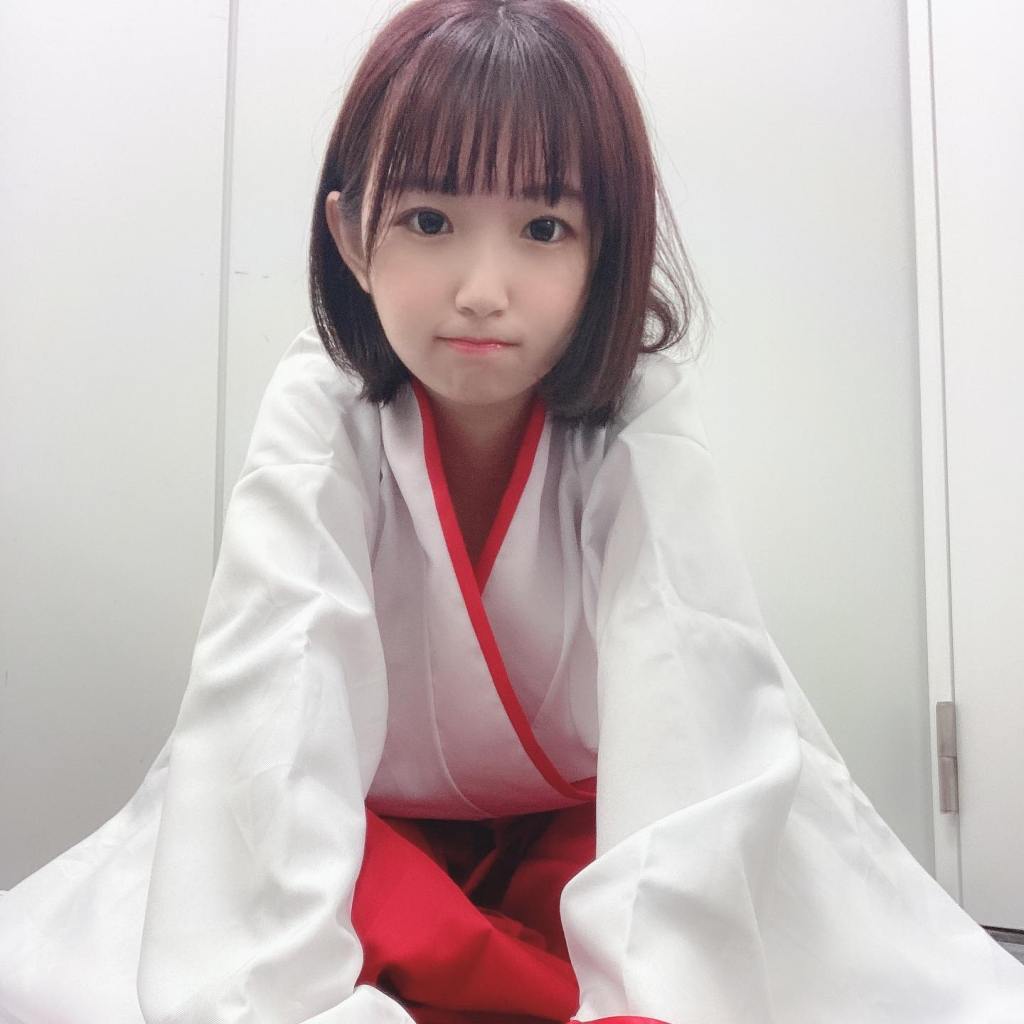 一名穿著白色和紅色傳統服裝的年輕女孩，坐在地上，面帶微笑，展現出可愛和迷人的姿態。