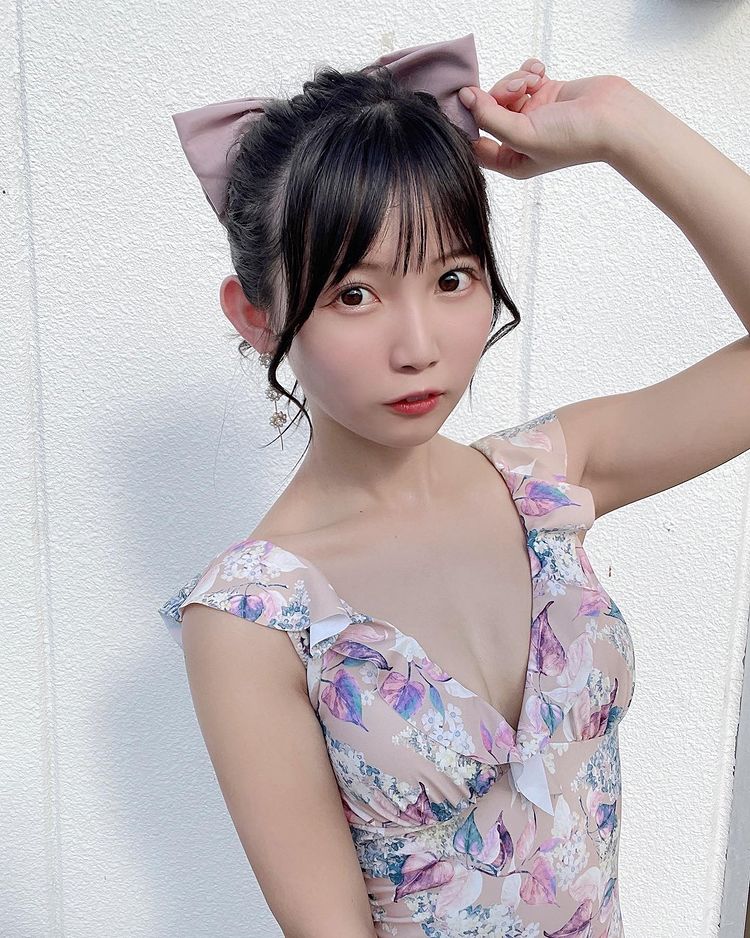 一位穿著花卉圖案服飾的年輕女性，手撥弄著頭髮，背景是淨白的牆面