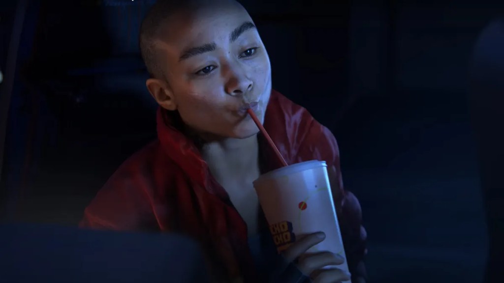 一位年輕女性坐在車內，穿著紅色外套，正喝著飲料，表情專注。