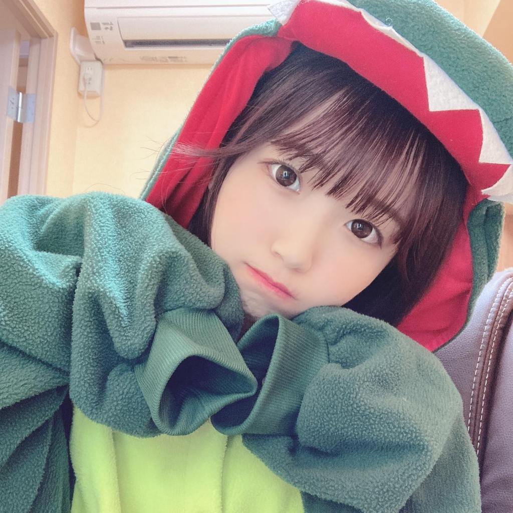 一個穿著恐龍連身衣的女孩，表情可愛，展現出無辜和俏皮的魅力，背景為室內環境。