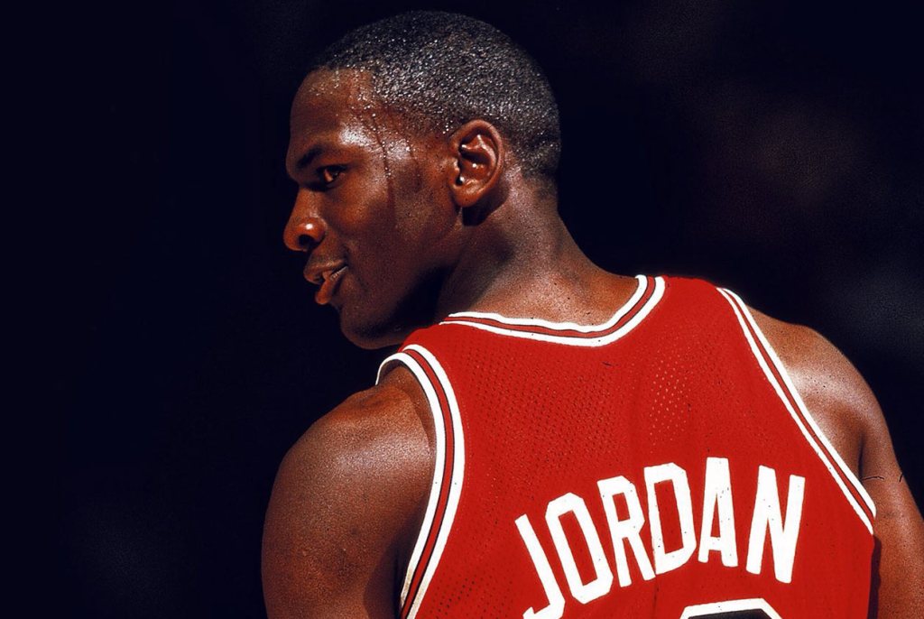一位身穿紅色籃球服的運動員，轉身面向鏡頭，背後的球衣上寫有'JORDAN'的字樣。
