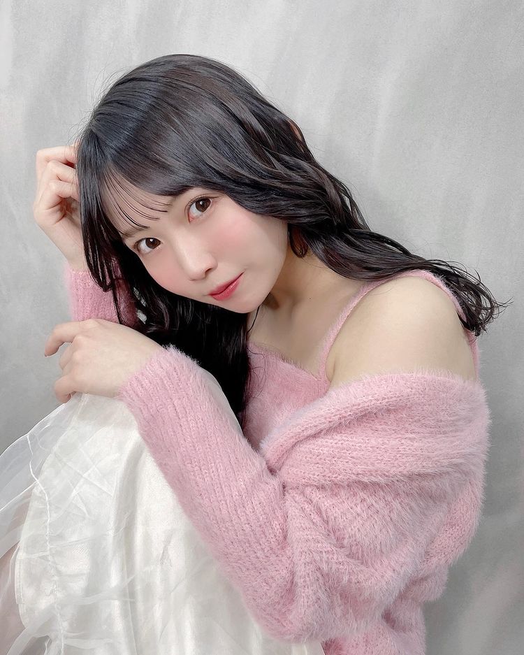 一位女孩穿著粉色毛衣，微笑著坐在柔和的背景前，展現出她的甜美和可愛的形象。