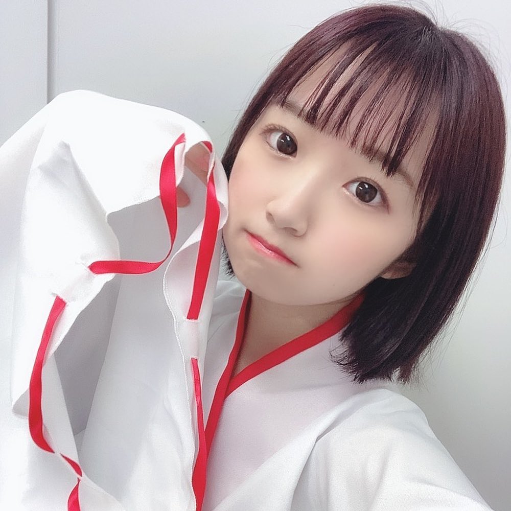 一名穿著白色衣服，手拿著衣服邊緣，展現可愛表情的女孩子。