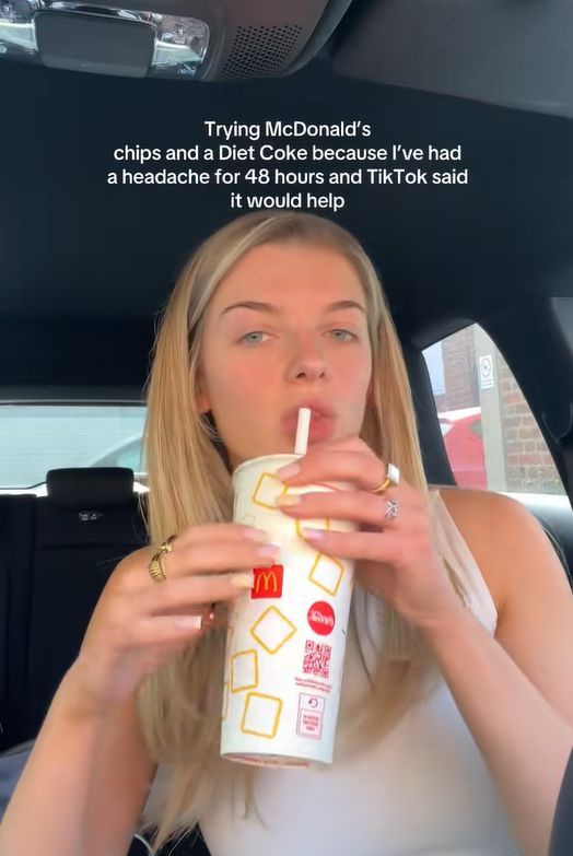 一位女性坐在車內，手中持有麥當勞的飲料杯，正喝著可樂，背景有車窗和其他車輛。