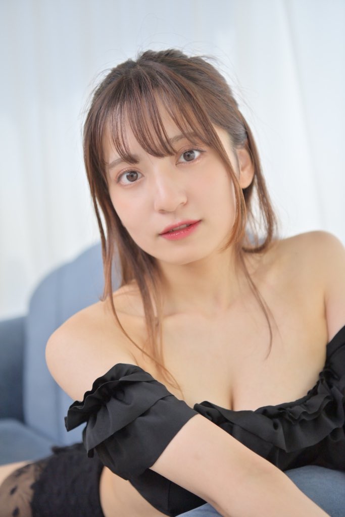 一位迷人的女性模特，穿著黑色的無袖上衣，坐在沙發上，微笑著面向鏡頭。