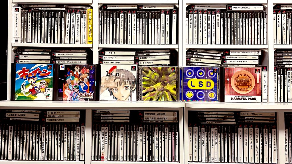 A collection of PlayStation 1 games displayed on shelves, featuring notable titles such as 'キューイン', 'Masters', 'i-Run', 'LSD', and 'Harmful Park'. The shelf is filled with neatly organized game cases.