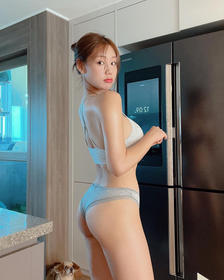 一位女性身穿灰色內衣，站在冰箱前，回頭看著鏡頭，展現優美曲線。