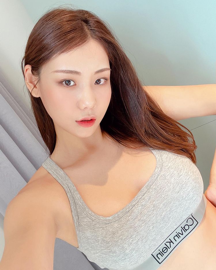 韓國女性穿著灰色運動內衣的自拍照，擁有自然的妝容和流暢的長髮，背景為柔和的色彩過渡。