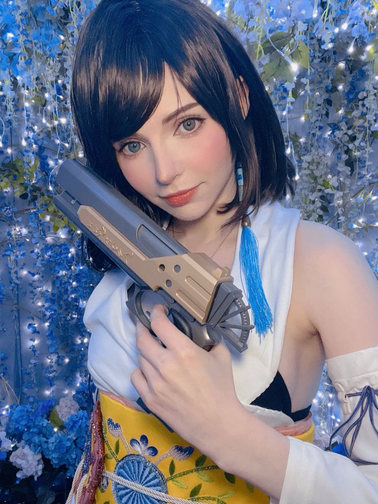 一位女性角色穿著色彩鮮豔的服裝，手持模擬武器，站在充滿燈光和花卉的背景前，展現出角色的特色與神態。