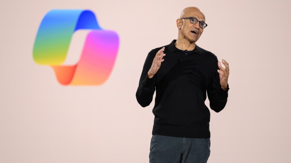 微軟CEO Satya Nadella 在舞台上發表演講，背景為呈現顏色漸變的標誌。