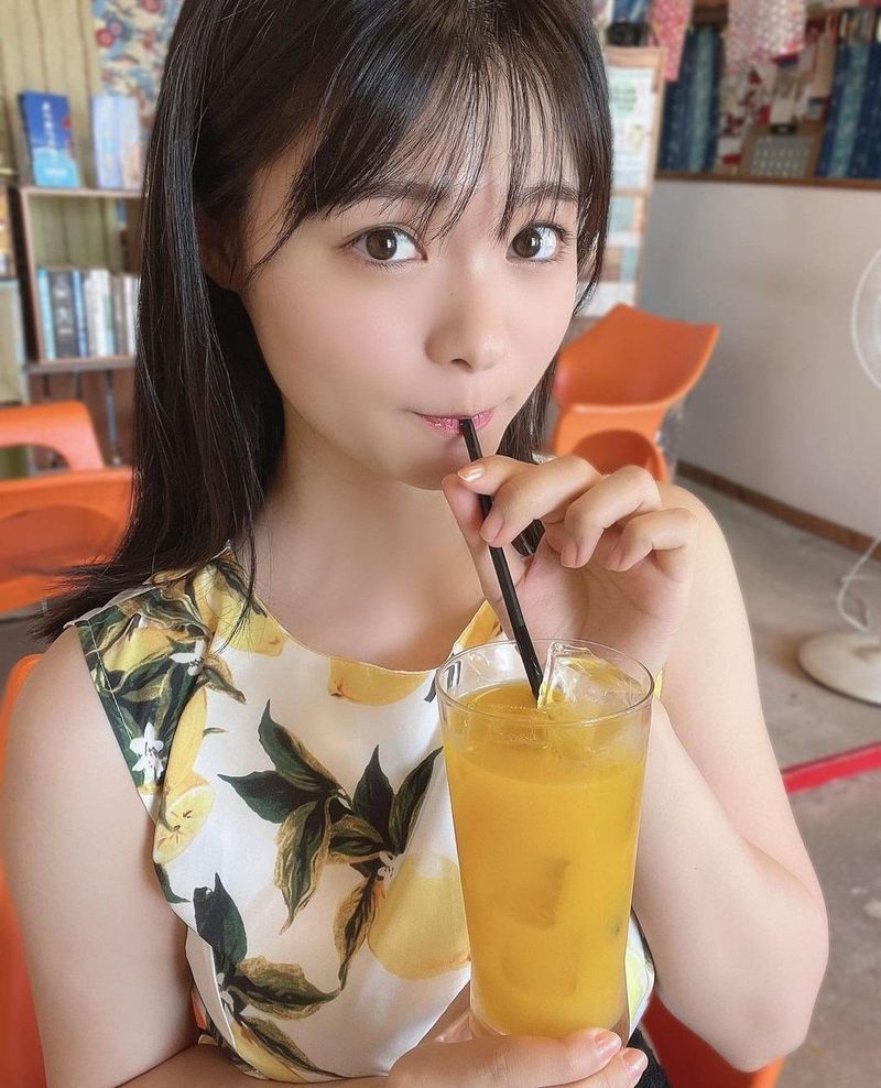 一位少女在飲用一杯橙色的飲料，穿著印有檸檬圖案的上衣，沉浸於愉悅的時光。