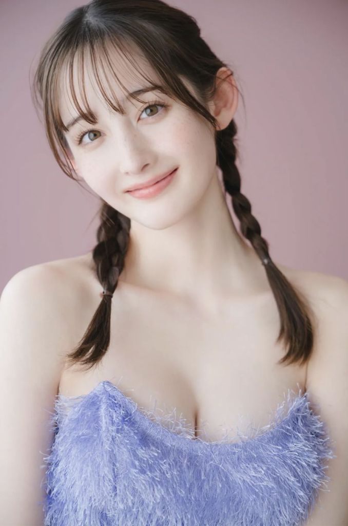 A young woman with braided hair smiles softly, wearing a fluffy purple top against a pastel pink background.