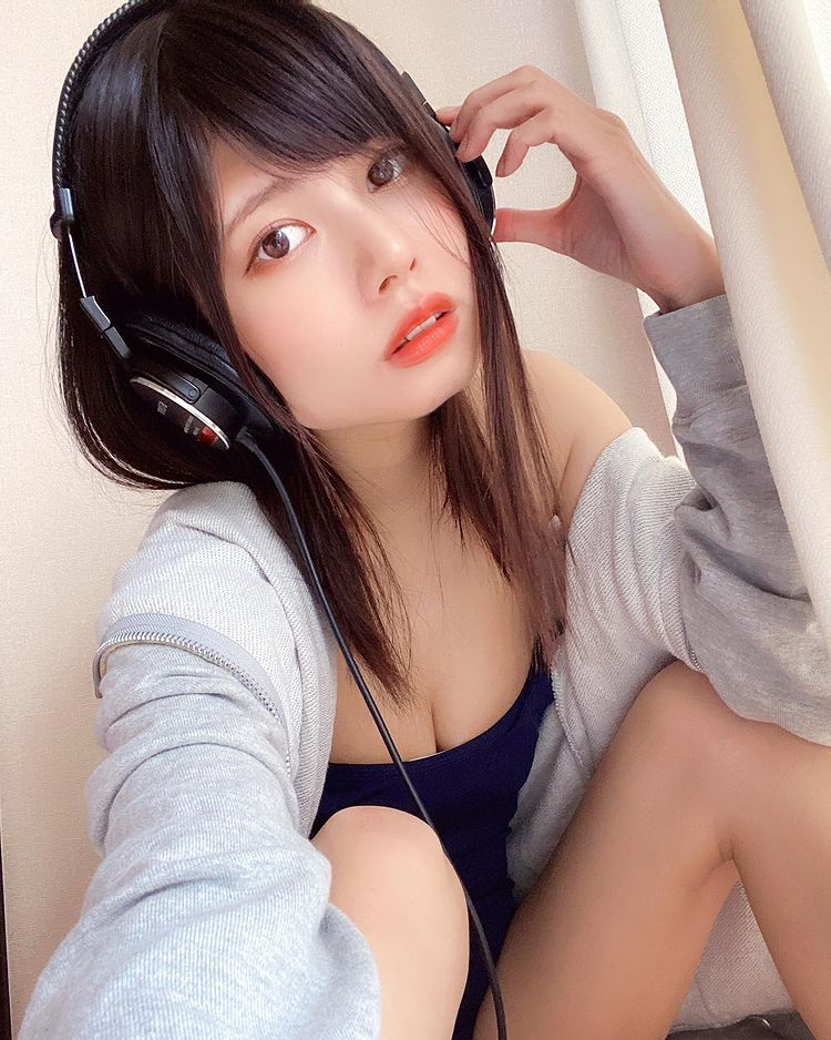 A young woman wearing headphones, sitting next to a beige wall with a light gray sweater draped over her shoulders.