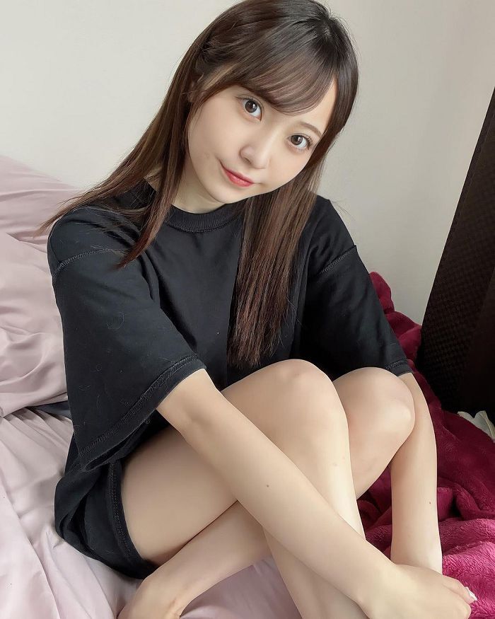 一名年輕女性坐在床上，穿著黑色 T 恤，微笑著看向鏡頭，背景為柔和的室內環境。