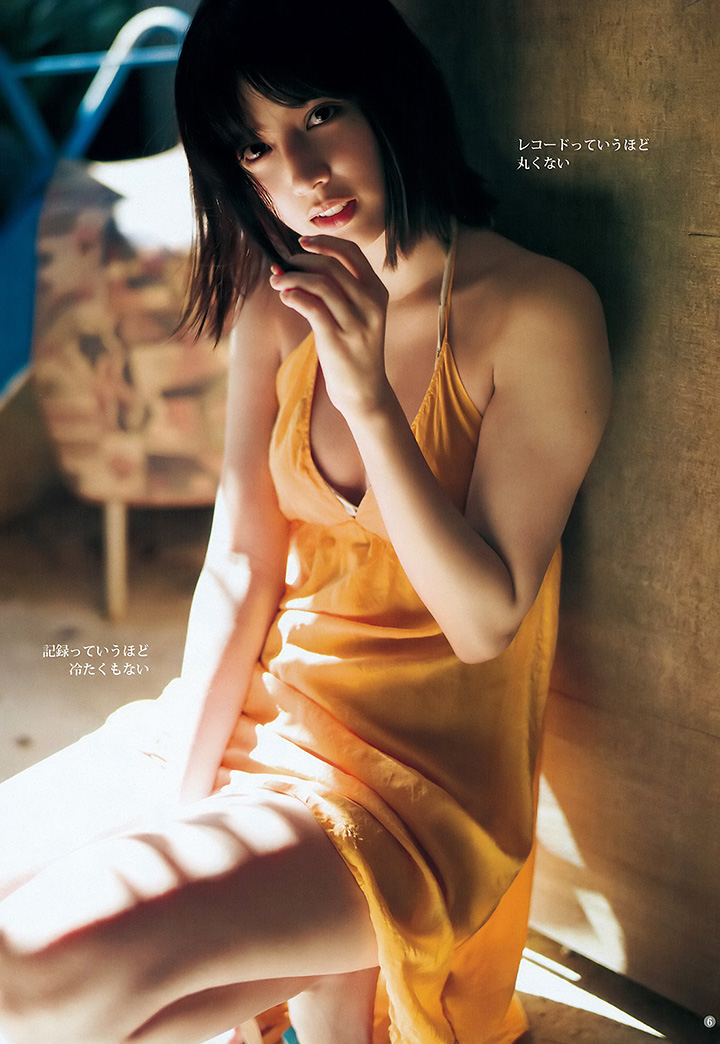 一位年輕女性穿著橙色裙子坐在室內，面帶微笑，姿勢自然，背景有光線透入。