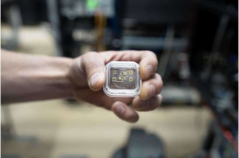 一名研究員手持一個透明容器，內放有新型光學原子鐘的元件，背景模糊顯示實驗室環境。