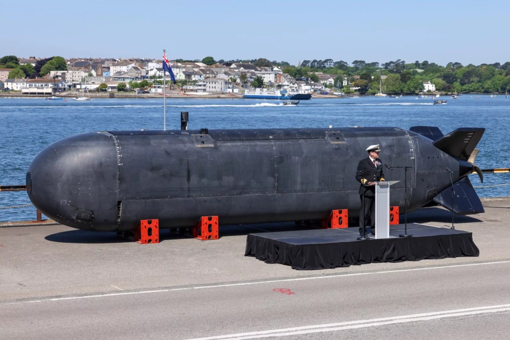 一名海軍上校在英國德文波特海軍基地面前的XV-Excalibur無人潛水器發表講話，背景是海岸線和其他船隻。