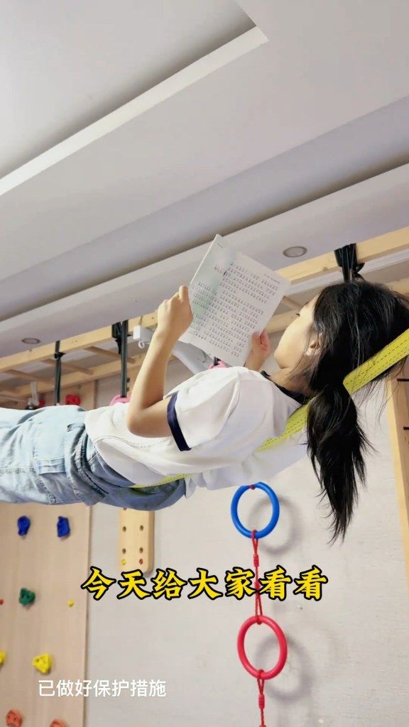 一位女孩在繩索上平穩躺臥，手中持著書本，展現出靈巧的閱讀姿勢。