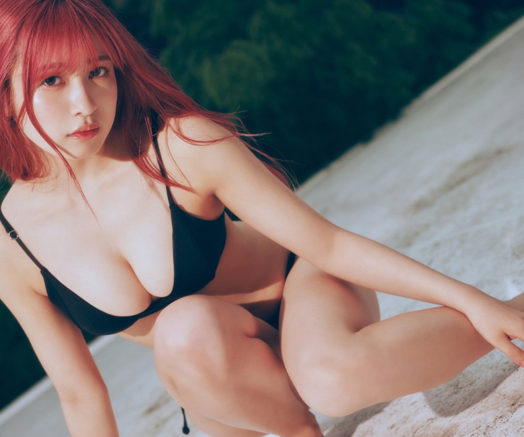 一位身穿黑色比基尼的女性在戶外沙灘上蹲下，背景為綠色植物，展現出自然的環境。