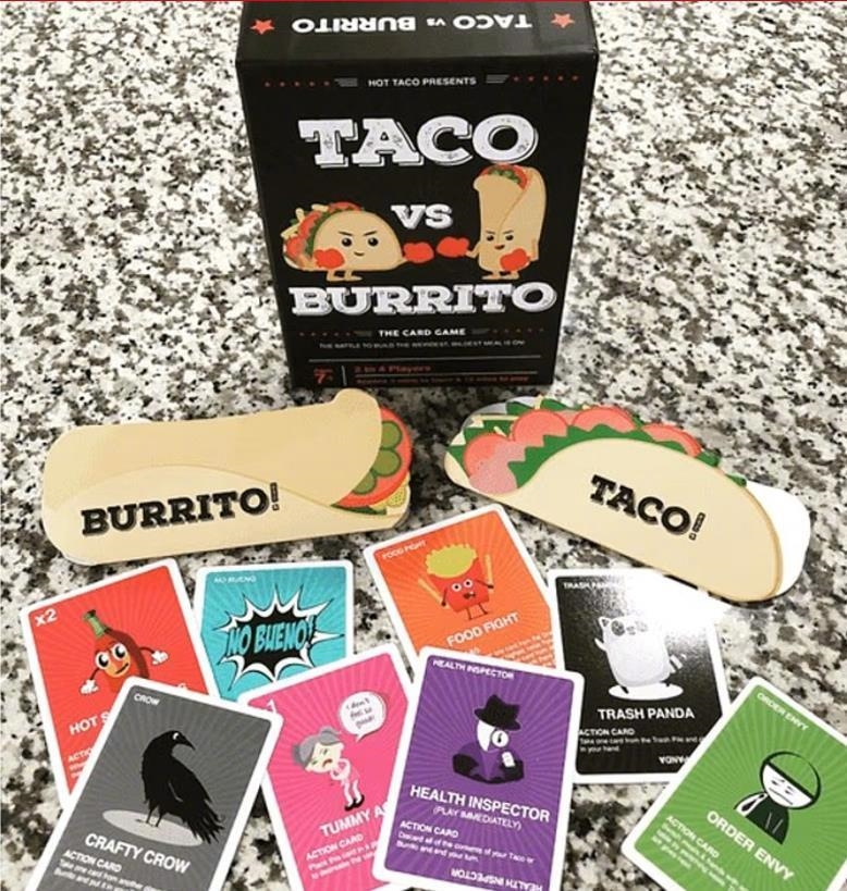 一個桌子上的紙牌遊戲《Taco vs. Burrito》，卡片和遊戲盒顯示了不同的角色和動作，包含"Burrito"和"Taco"的標籤。