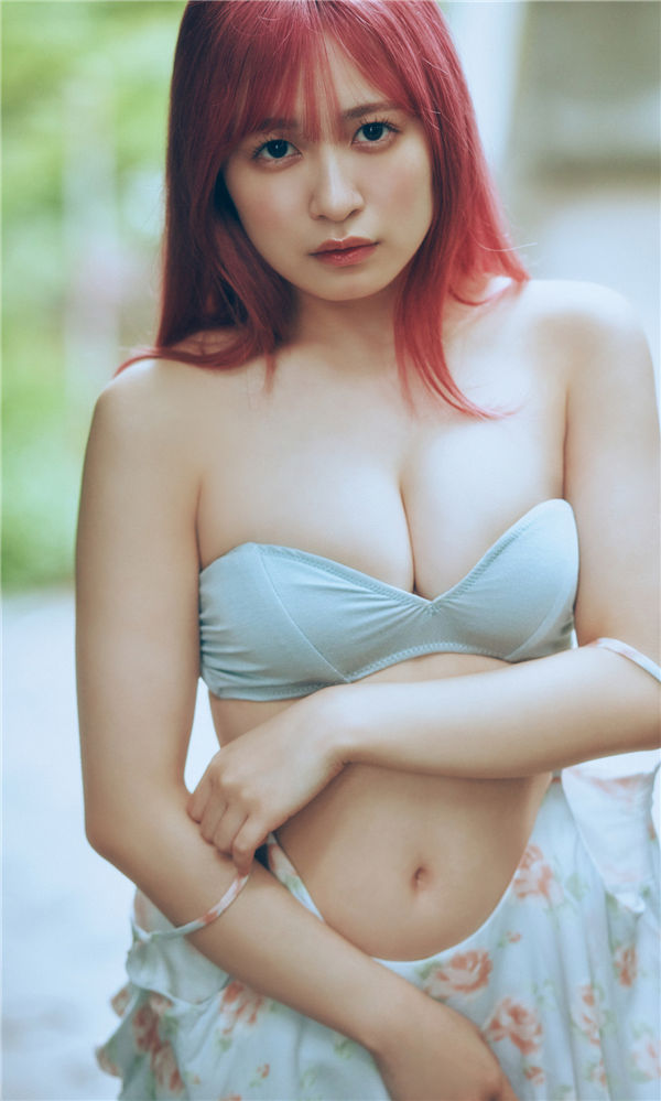 一位女性穿著淺藍色上衣和花裙子，展現迷人的姿態，背景為模糊的綠色自然景觀。