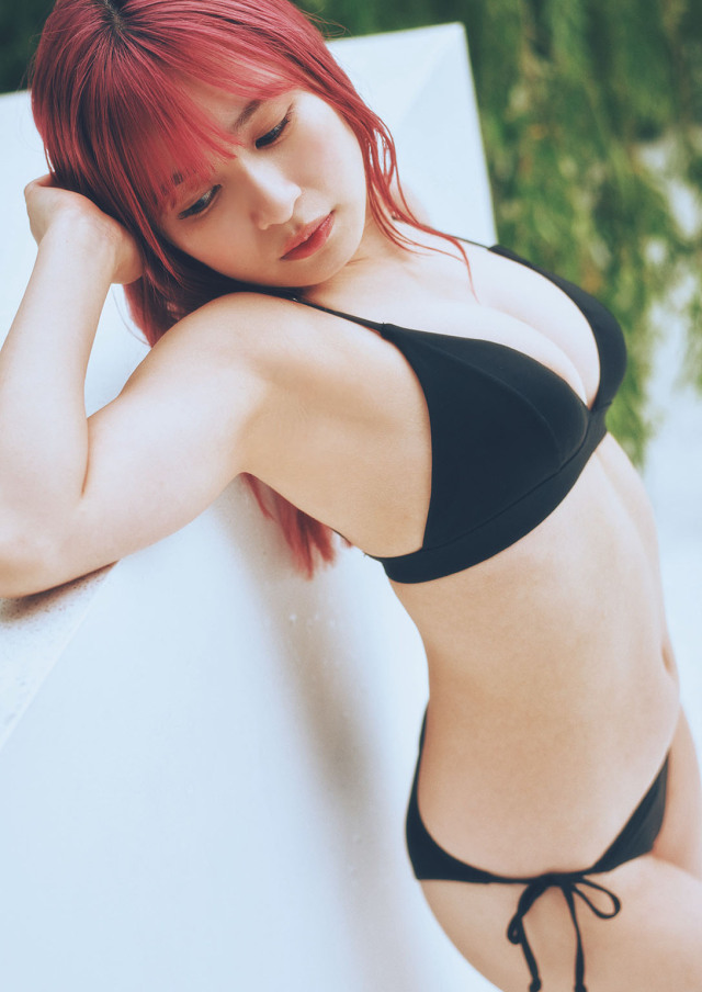 一位擁有粉紅色頭髮的女性，穿著黑色比基尼，靠在牆上展現魅力，背景為綠色植物，捕捉了清新與性感的氛圍。