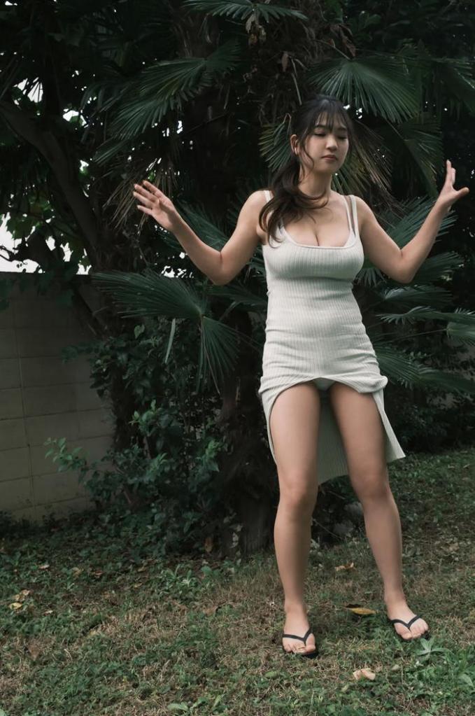 A young woman in a light-colored dress standing in a grassy area with palm trees in the background.