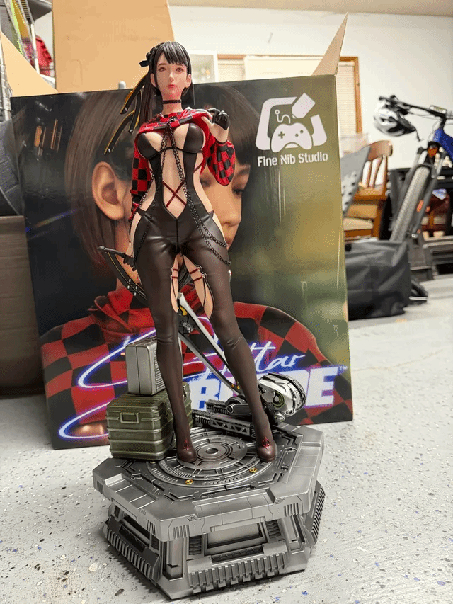 一個手辦模型，展示了一位身穿紅黑格子衣服的女性，站在一個圓形平台上，背景是手辦的包裝盒，地面為水泥質地。