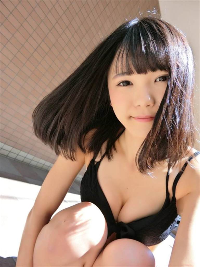 A young woman with shoulder-length black hair is smiling while posing in a black top in a well-lit indoor setting.