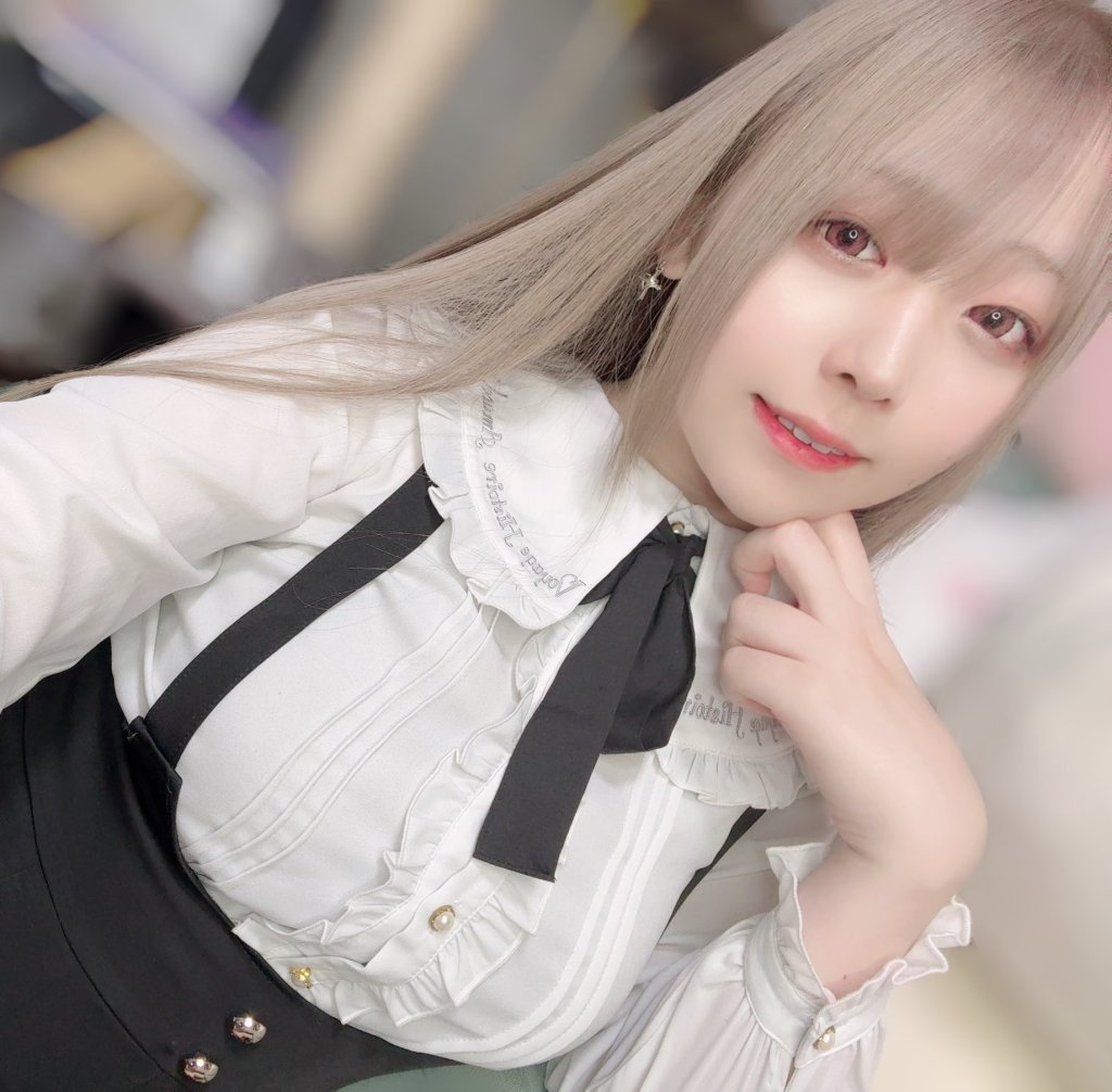 A person with long light hair wearing a white shirt with ruffles and a black bow tie, posing for a selfie.