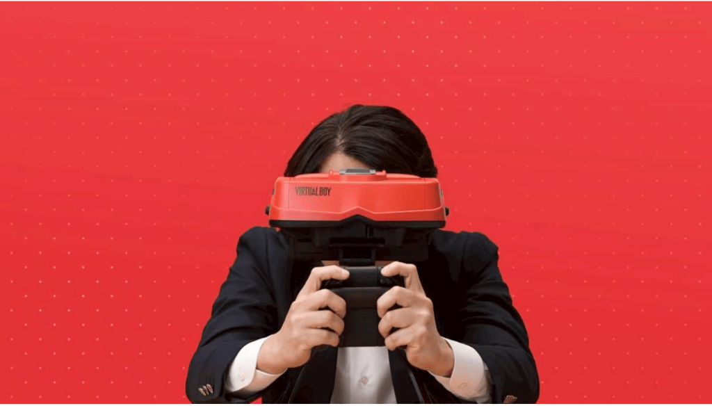 一名男性穿著西裝，手持Virtual Boy遊戲機，背景為紅色。