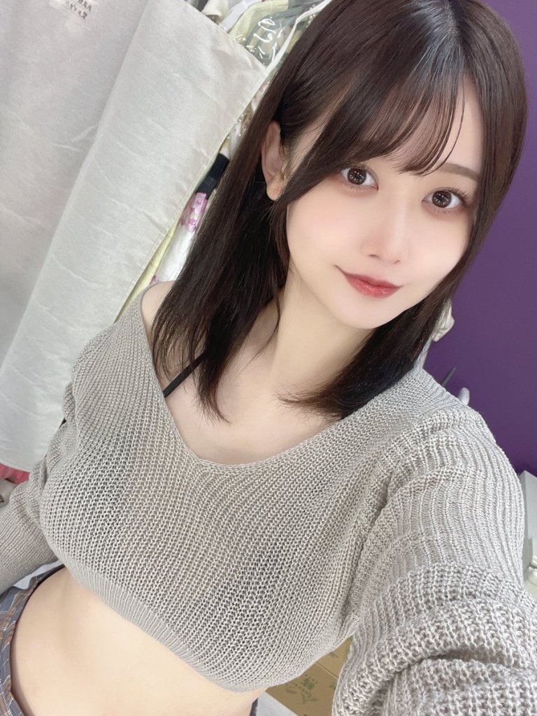 Young woman smiling in a gray off-the-shoulder sweater against a purple background.