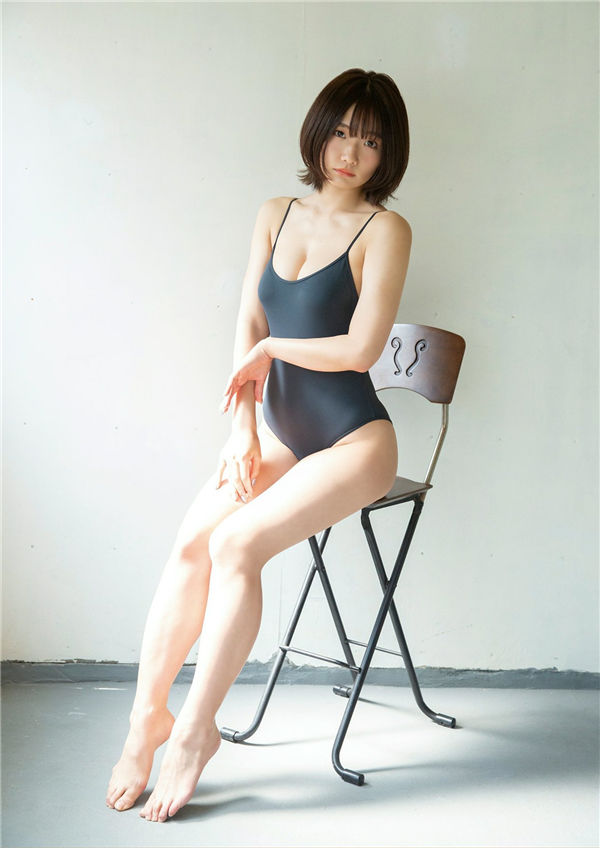 A person sitting on a chair wearing a black swimsuit, showcasing a minimalist and relaxed pose in a well-lit indoor setting.