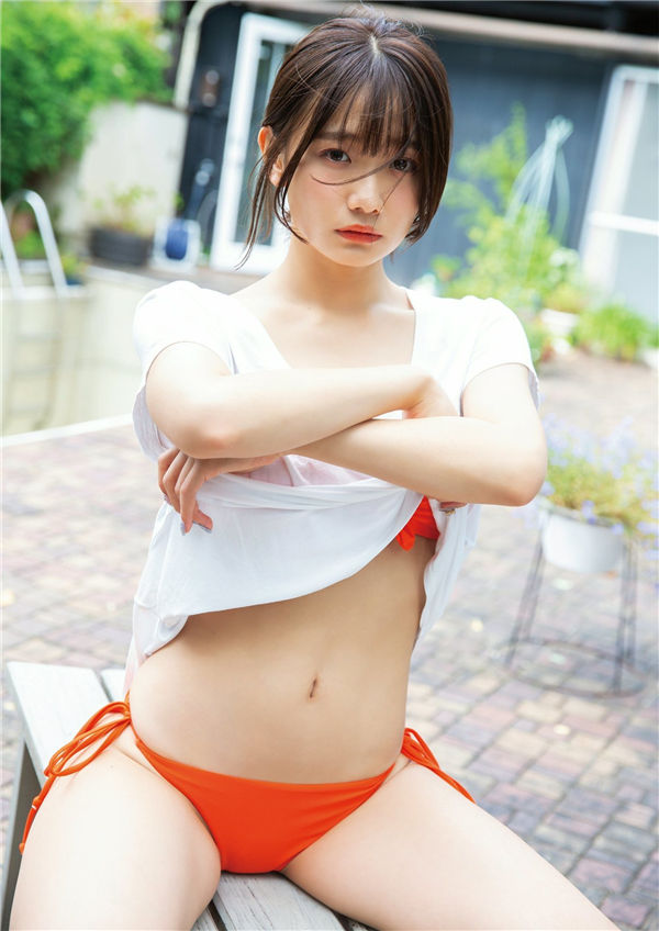A young woman posing with her arms crossed, wearing an orange bikini bottom and a partially open white shirt, set in a garden-like background.