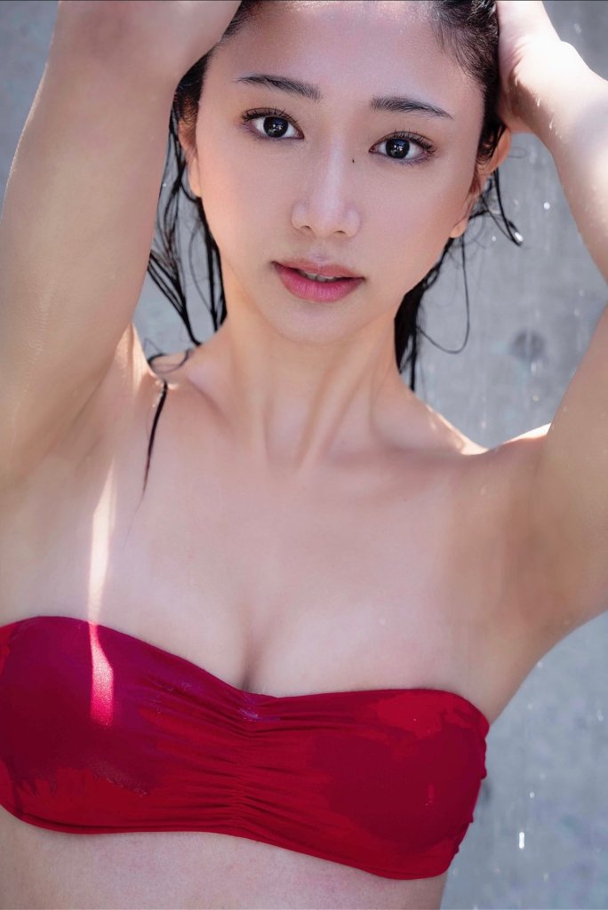 Close-up portrait of a woman with wet hair, wearing a red strapless top, looking directly at the camera with a soft expression.