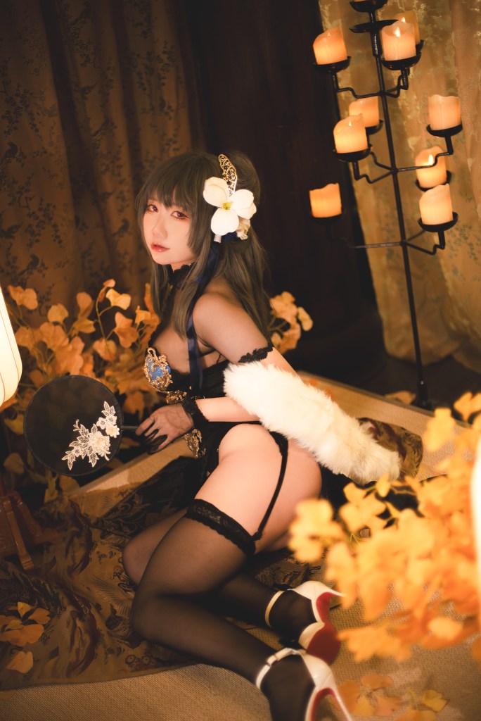 A woman in elegant attire posed in a beautifully decorated room with candles and flowers, wearing a flower accessory in her hair.