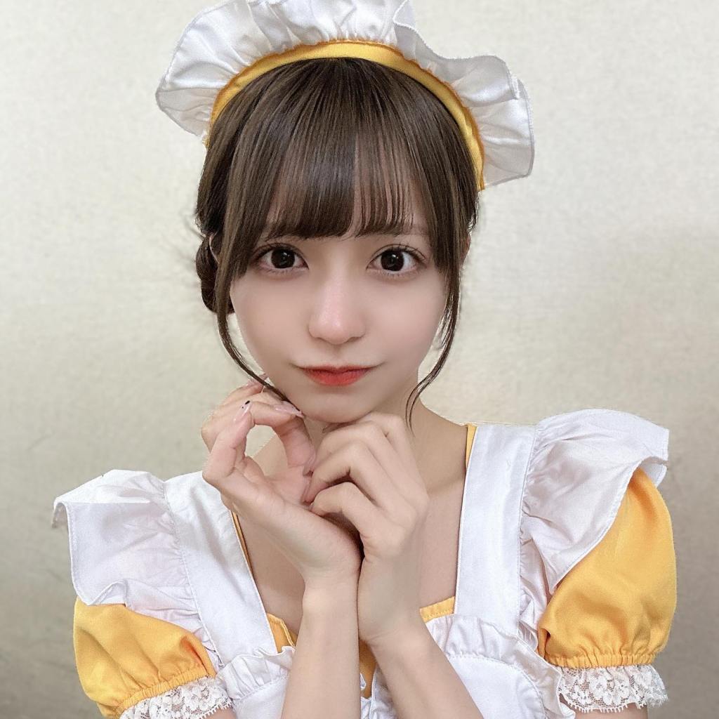 A young woman wearing a maid outfit with a yellow and white color scheme, posing with her hands near her face and a playful expression.