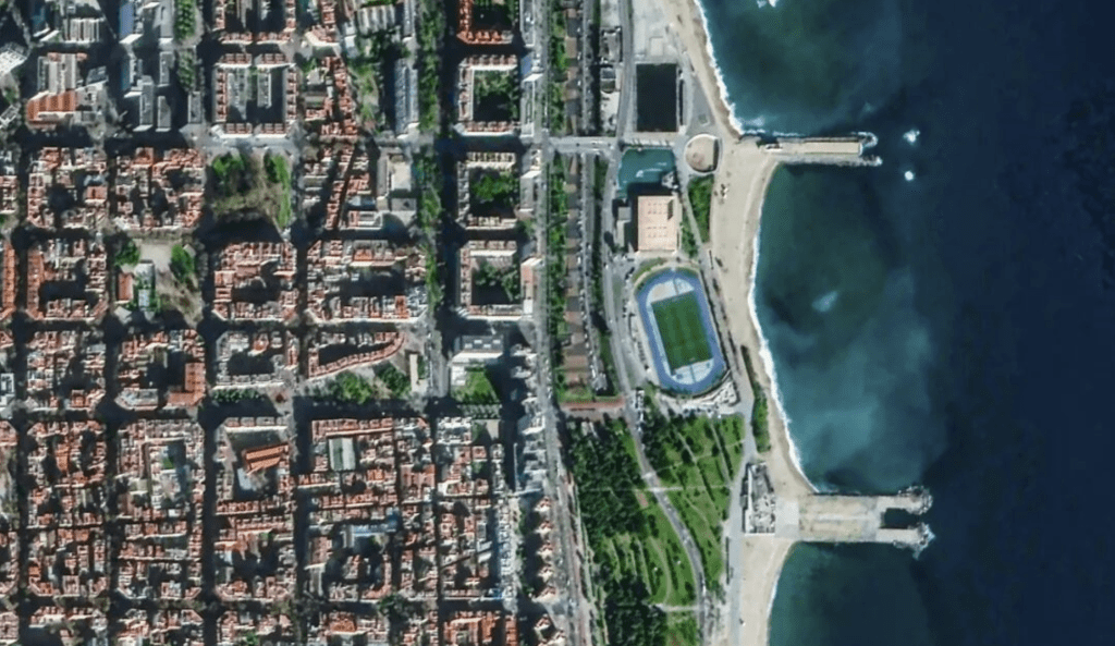 衛星視角下的巴塞隆納擴展區,展示規整的棋盤格街區和海岸線,顯示城市規劃的特色和結構。