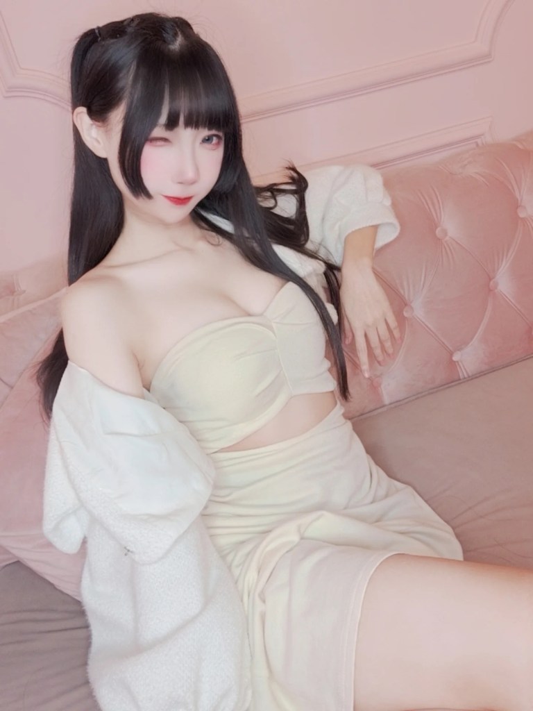 一位穿著淺色服裝的女性，坐在粉紅色沙發上，微笑並眨眼。背景柔和，增添了溫馨的氛圍。