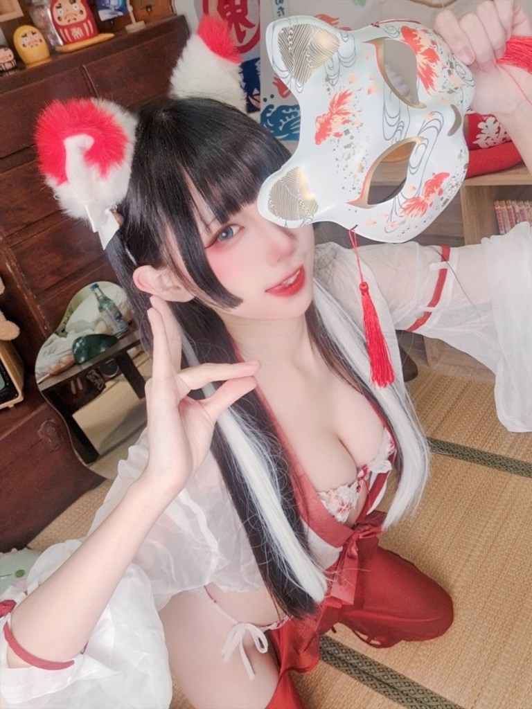 一位穿著紅色和白色服裝的女生，手持一個裝飾著魚圖案的面具，面帶微笑，背景有傳統的日本風格裝飾。