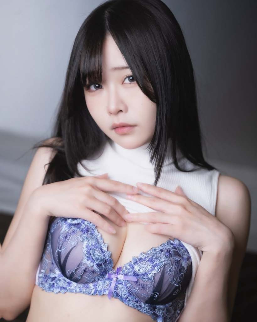 一位女性模特穿著紫色蕾絲內衣，低頭看向鏡頭，手輕觸胸前，背景柔和且模糊。