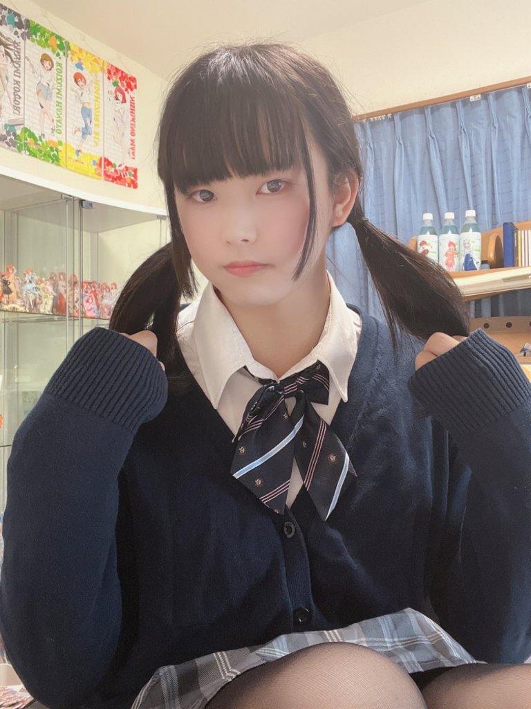 一位穿著校服的年輕女性，手上捏著雙馬尾，坐在室內，背景中可見一些玩具和瓶裝飲料。