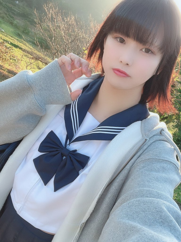 一位穿著水手服和灰色外套的年輕女性自拍，背景為自然環境，光線柔和。