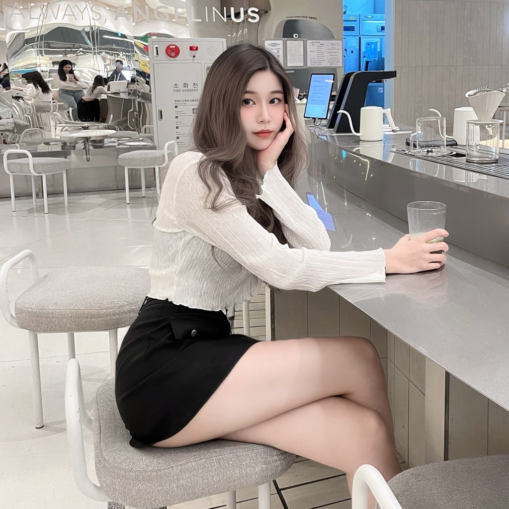 一位女生坐在咖啡廳的吧台前，穿著白色上衣和黑色裙子，手中拿著一杯飲料。