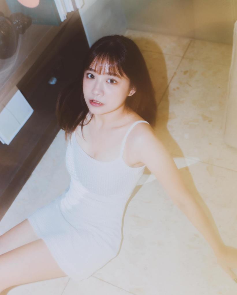 一位年輕女性穿著白色連衣裙坐在地板上，背景含有書架和柔和的光線效果。