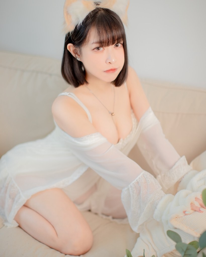 一位女性坐在沙發上，穿著白色的蕾絲衣物和可愛的耳朵髮飾，表情恬靜。