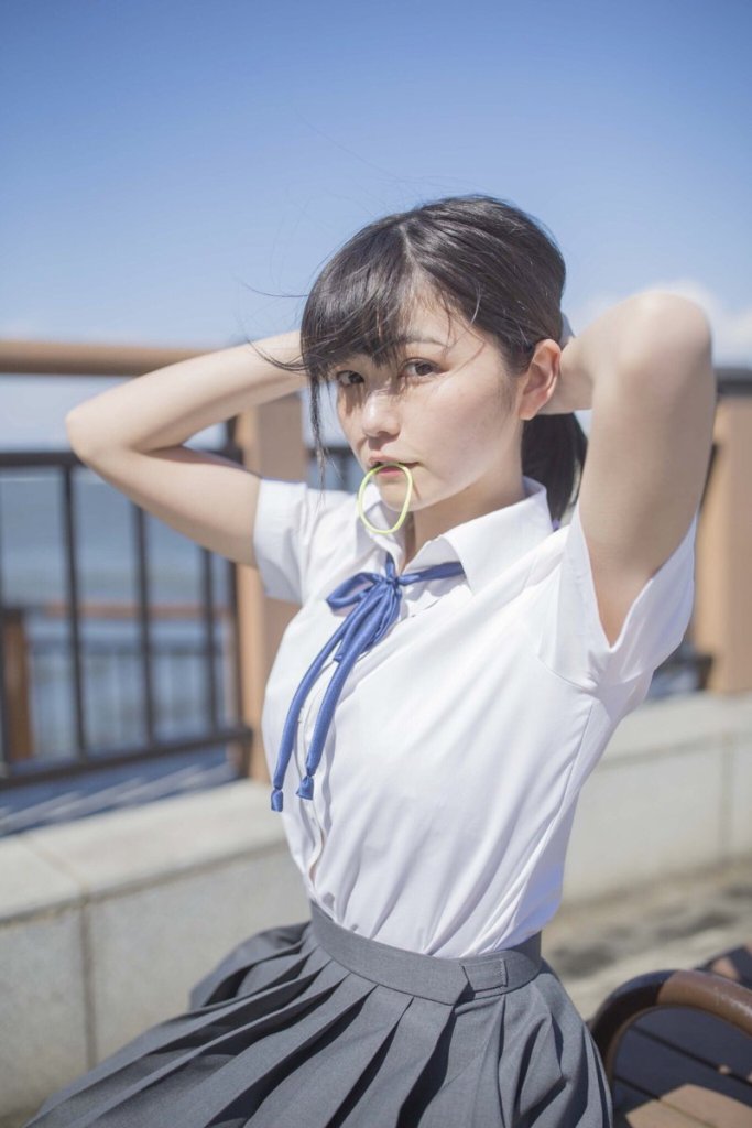 一位年輕女性在陽光明媚的戶外，穿著白色襯衫和灰色裙子，正在整理頭髮，嘴裡含著橡皮筋。